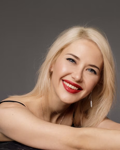 a blonde woman smiling at the camera with pearly whites and red lips
