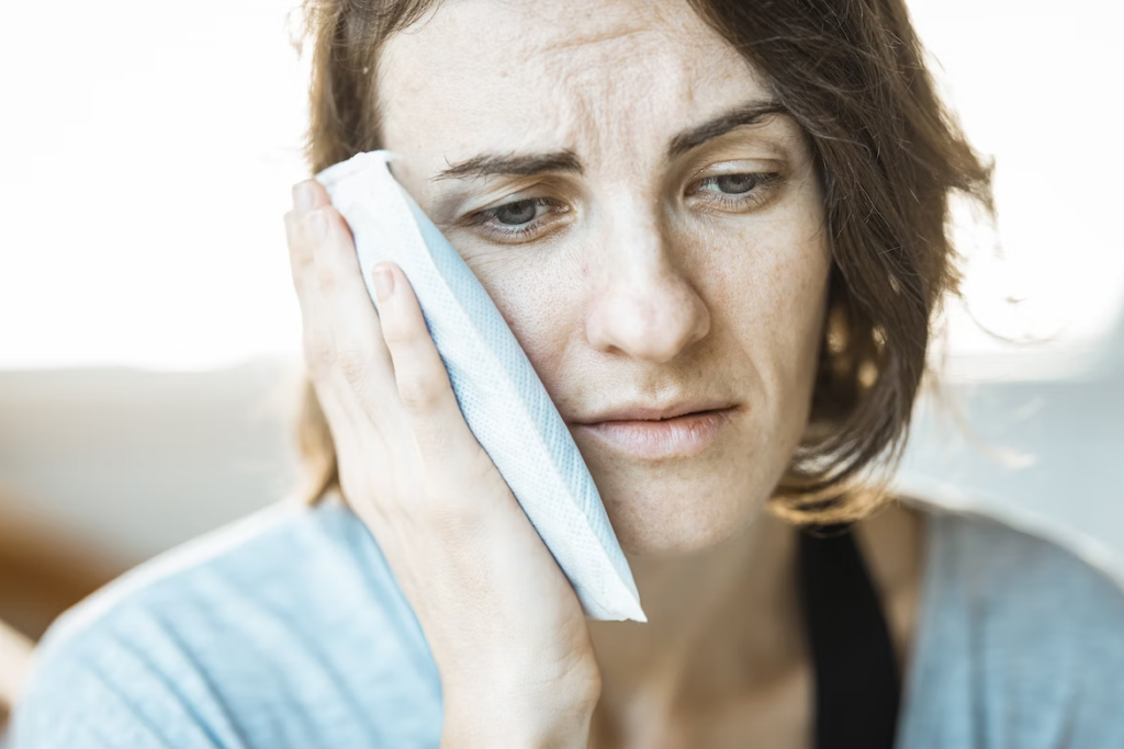 a woman frowning in pain while holding a compress to her jaw