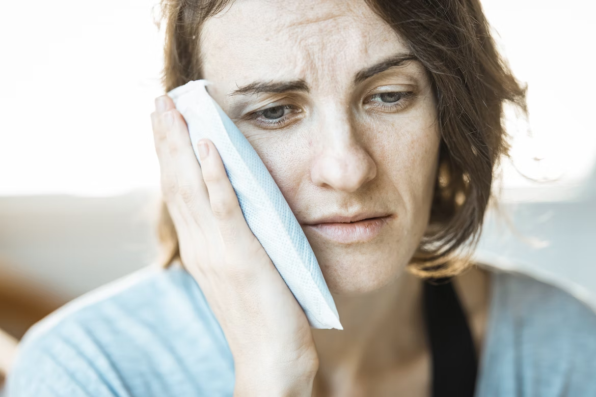 a woman frowning in pain while holding a compress to her jaw